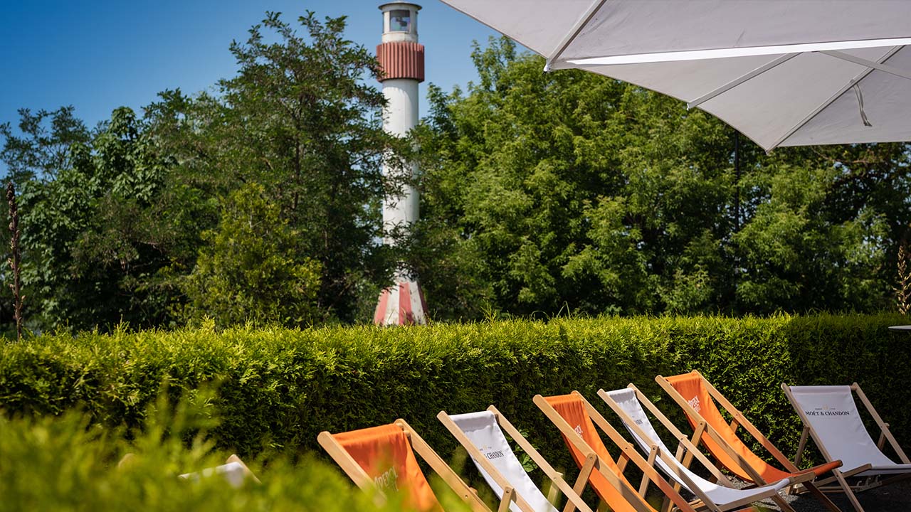 Weiße und orangefarbene Liegestühle unter weißen Sonnenschirmen, eingerahmt von einer halbhohen Hecke und bewacht von unserem Leuchtturm - hier kann man wunderbar entspannen.