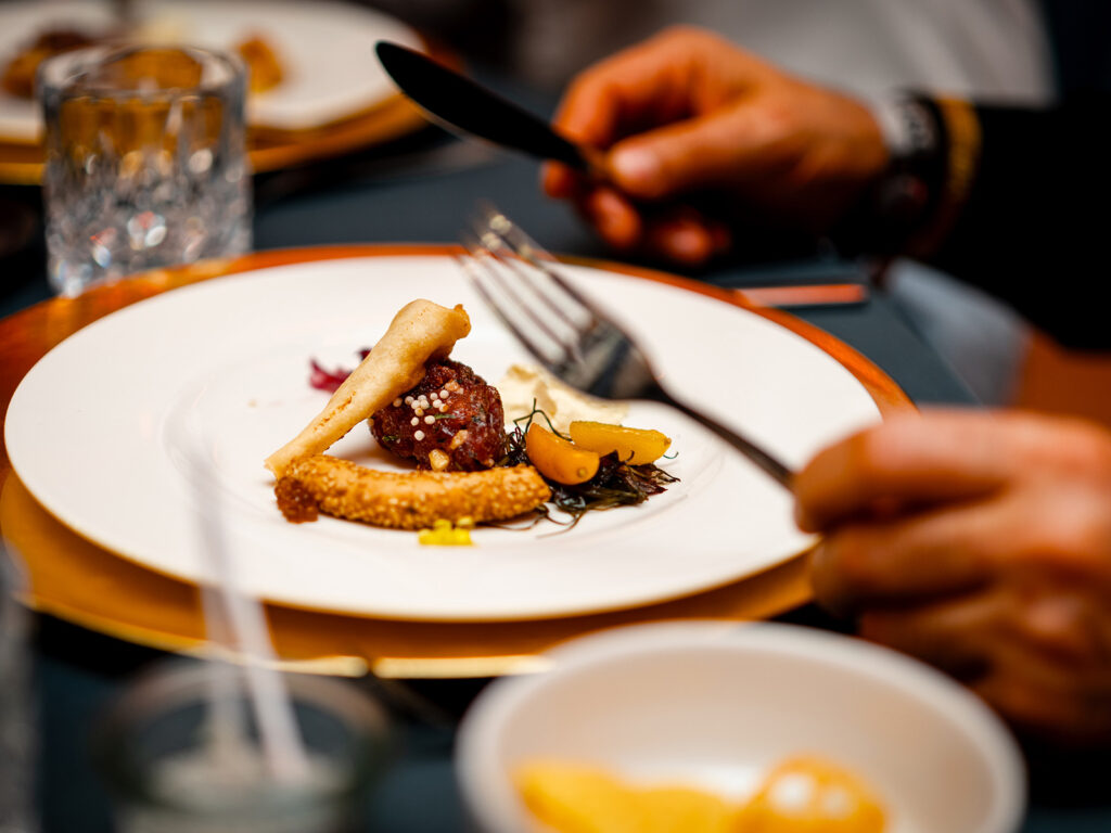Finedining - Nahaufnahme eines Tellers, davor eine Person mit Besteck in der Hand
