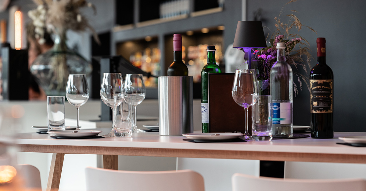 Gedeckter Tisch mit Gläsern, Wein- und Wasserflaschen.